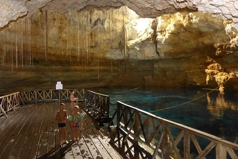 Swimmers on a wooden deck beside a cave cenote on a Cobá and Tulum day trip from Playa del Carmen, Mexico